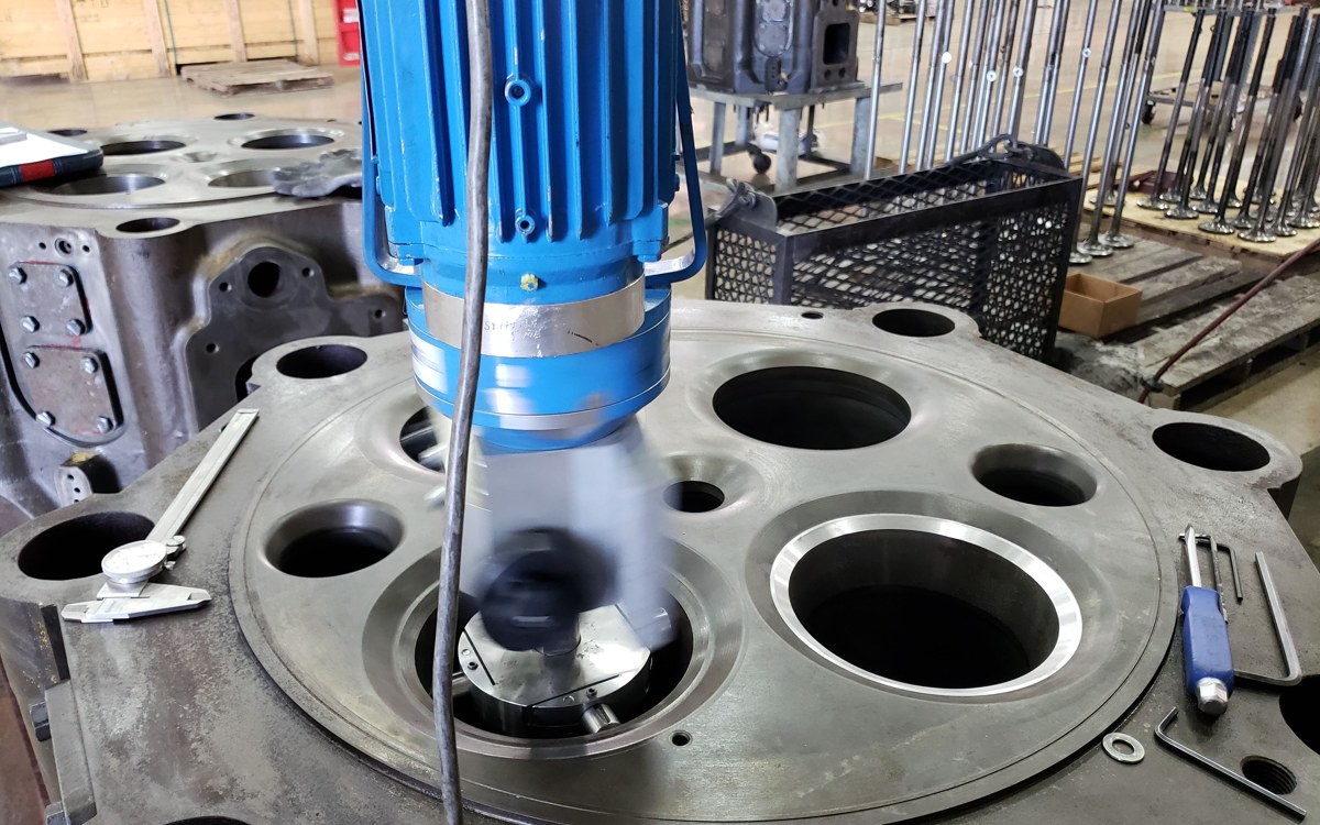 Portable machining unit set up over the marine cylinder head with dial indicator and gauges staged for seat checks